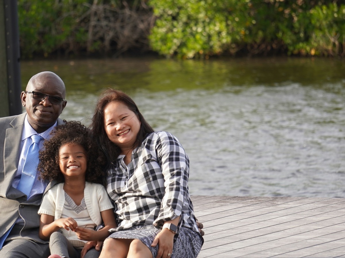 A family of three sitting together beside a lake