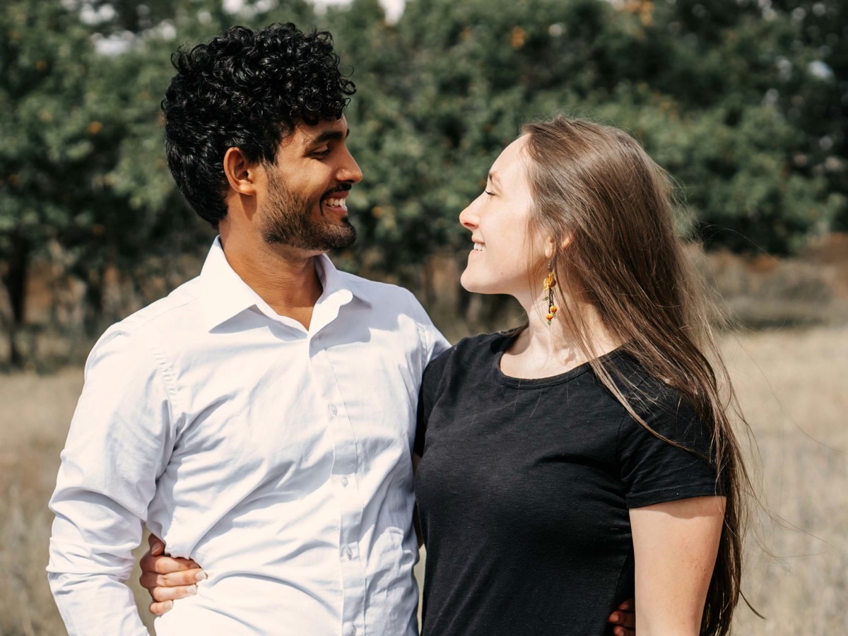 Una pareja de pie, muy juntos al aire libre, mirándose